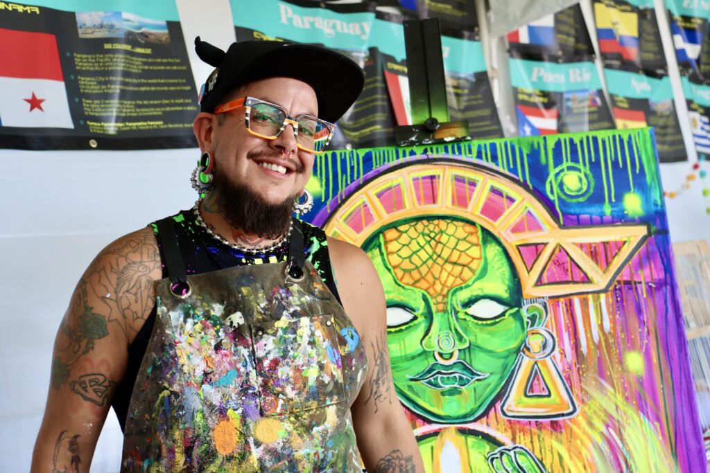 Artist Tino Lopez stands next to his artwork inspired by Indigenous Peoples’ Day at Latino Village
