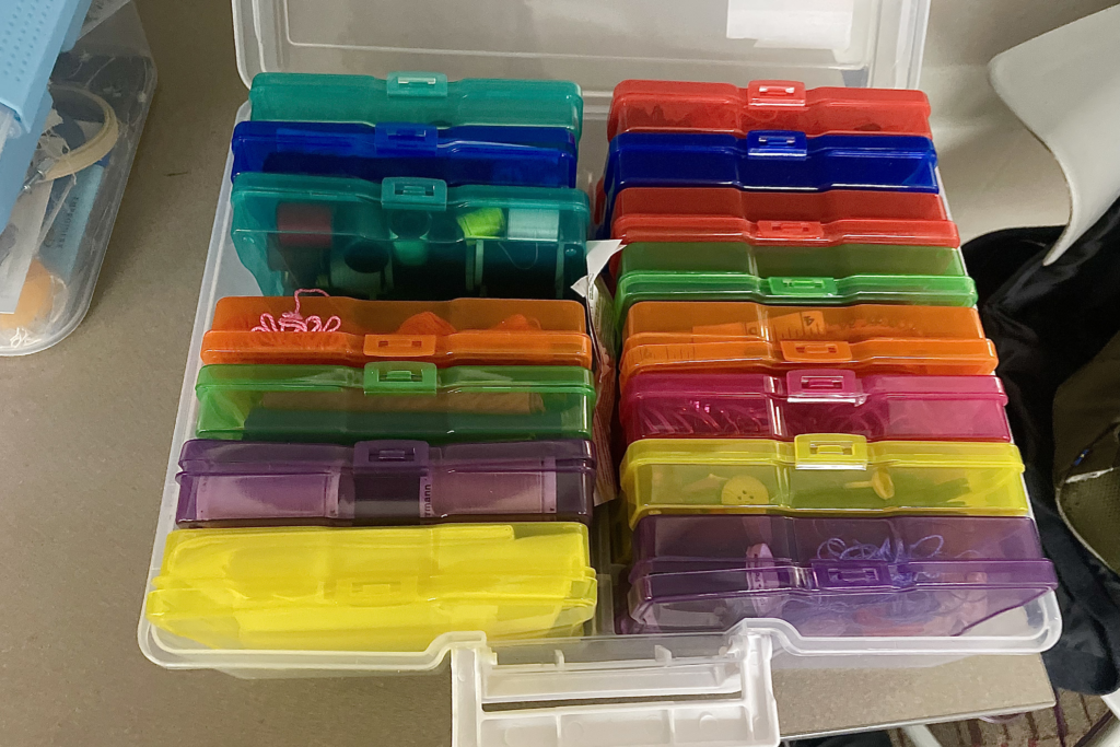 In a clear white box on a table sits a multitude of color pencil cases filled with crafting supplies.