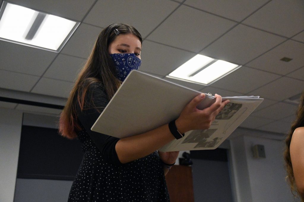 Valerie Goldstein reading lines from a script in a white binder.