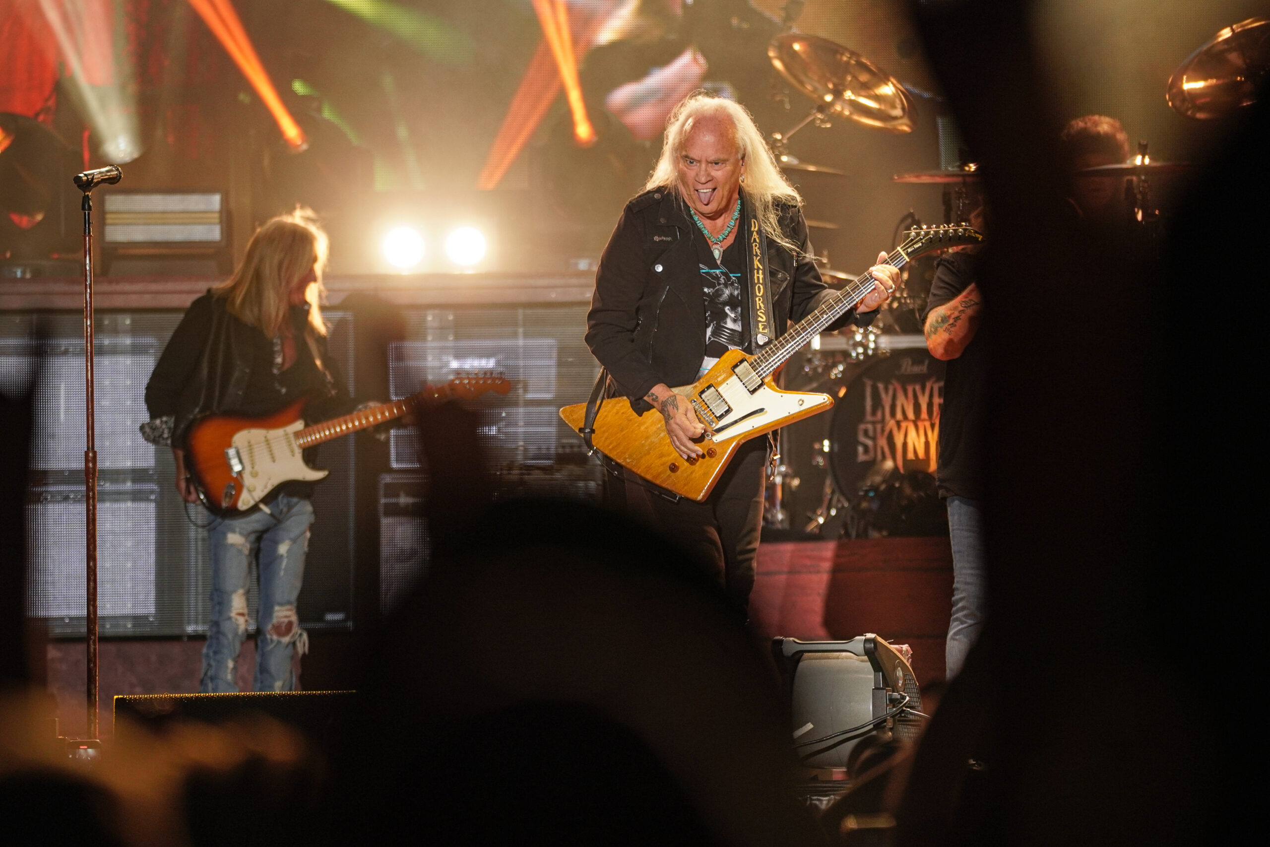 A member of Lynyrd Skynyrd sticks out his tongue at the crowd while holding an orange guitar