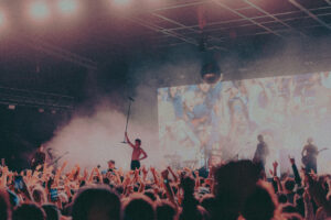 A crowd raises up rock and roll signs as a performer holds up his microphone stand