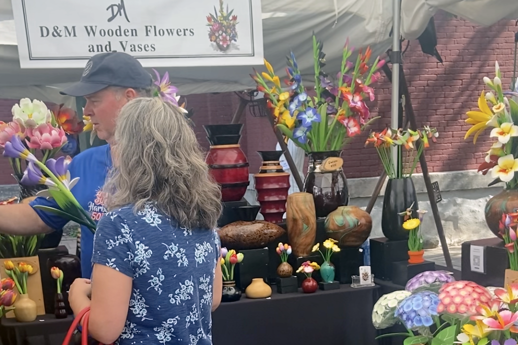 Mike Miller, one half of D&M Wooden Flowers and Vases, interacts with a customer in their stall at the Syracuse Arts & Crafts Festival in downtown Syracuse.