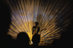 Yellow beams of light streak behind Gregory Alan Isakov, whose sillhouette shows him holding a guitar and singing into a microphone. Gregory Alan Isakov’s setlist spanned his six albums, including songs from his Grammy-nominated Evening Machines and latest release, Appaloosa Bones.