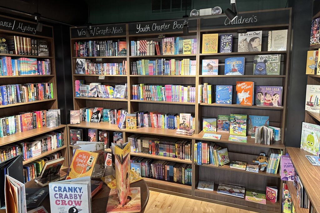 A large wooden bookshelf sits against a wall featuring dozens of colorful books stacked on the shelves.