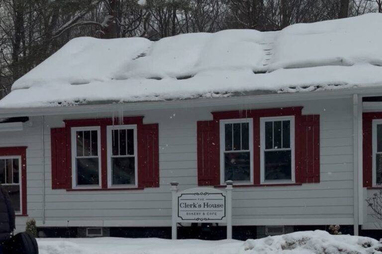 A building with red and white exterior and a snowy front have a bakery and cafe sign out front.