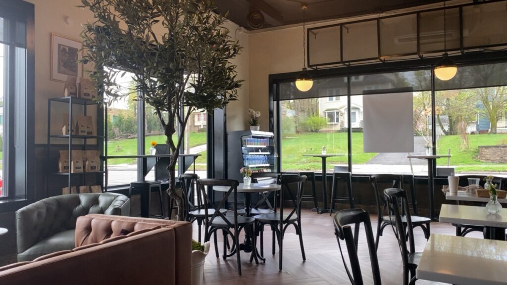 An interior of a coffee shop with a chairs, tables, and set of couches with large windows in the back.