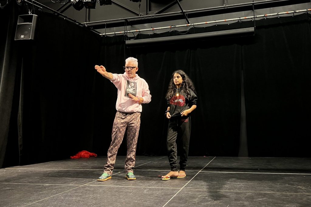 José Miguel Hernandez-Hurtado and Ahitana Garcia-Rodriguez stand on an empty black stage, with Hernandez-Hurtado motioning a stage direction for Garcia-Rodriguez.