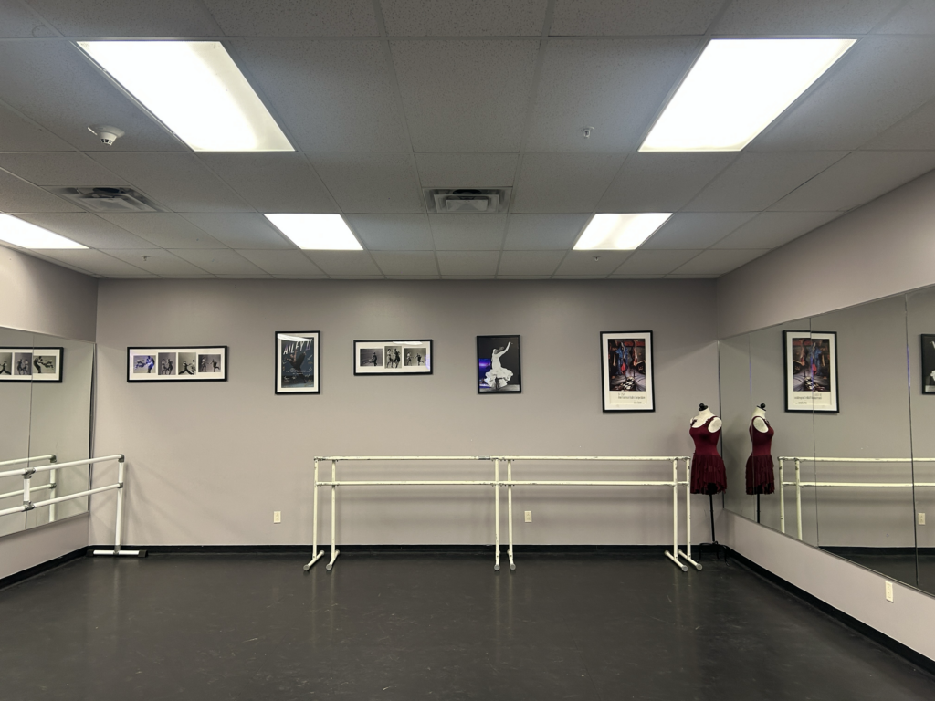 A dance studio with a bare, photos on wall and a mirror.