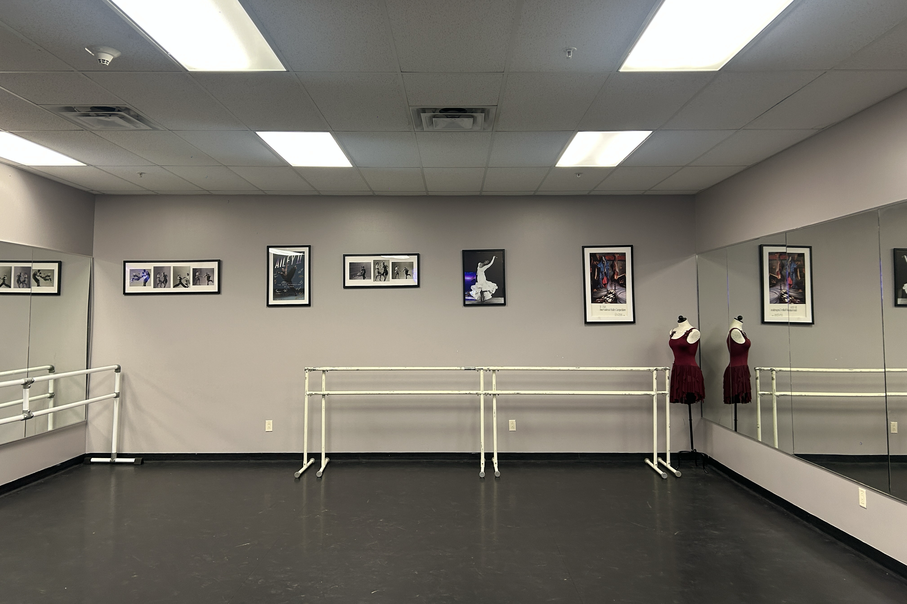 A dance studio with a bare, photos on wall and a mirror.