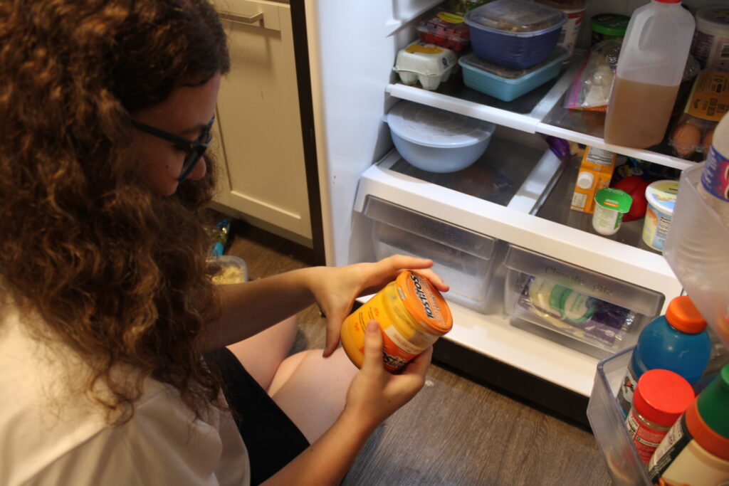 Caroline Cornely examines a jar of Tostitos cheese dip during a fridge clean-up in her Syracuse apartment.