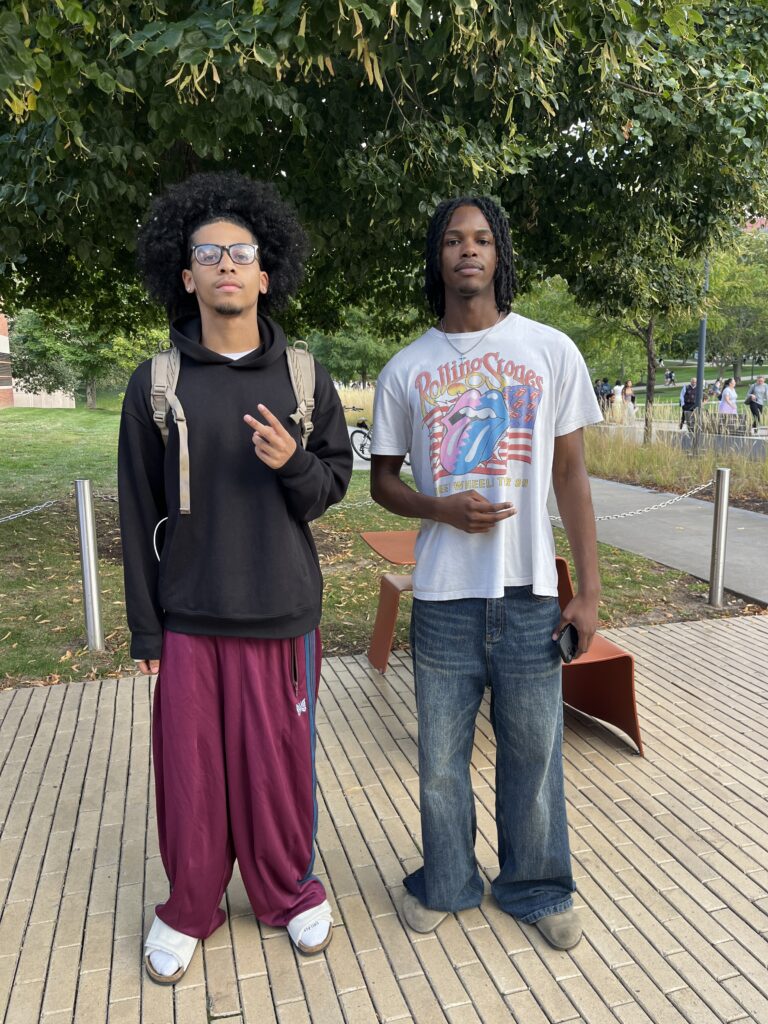 Sports Management freshman majorIsaiah stands in a black sweatshirt next to freshman Film major Logan Pierre in band t-shirt.