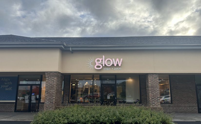 Exterior view of Glow Yoga and Juice, a storefront with a pink sign and brick accents.