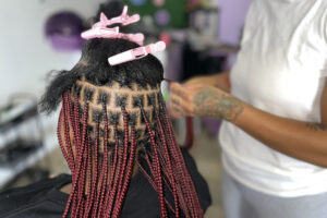 Gabrielle Lloyd, owner and stylist at the Divine Den in Syracuse, braids a client’s hair into medium knotless braids.