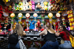 Fair attendees sit at a fair-game stand surrounded by stuffed-animal prizes.
