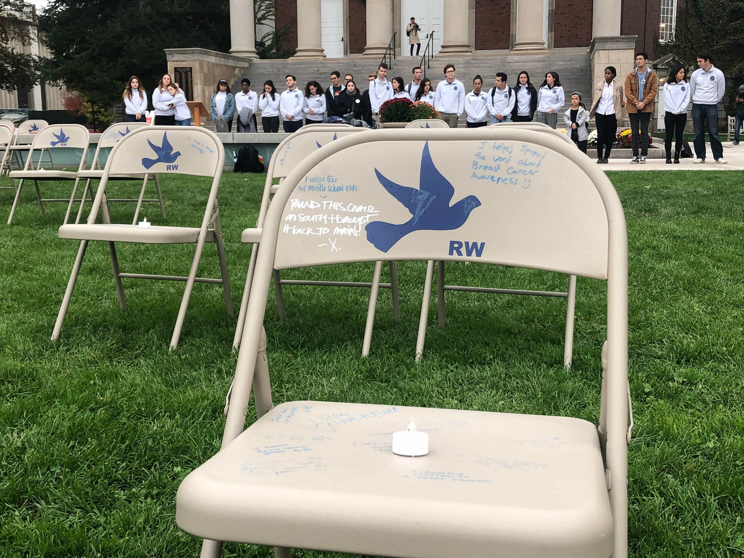 The emotional scholars stand in silence, looking at the glowing candles on the 35, now empty chairs.