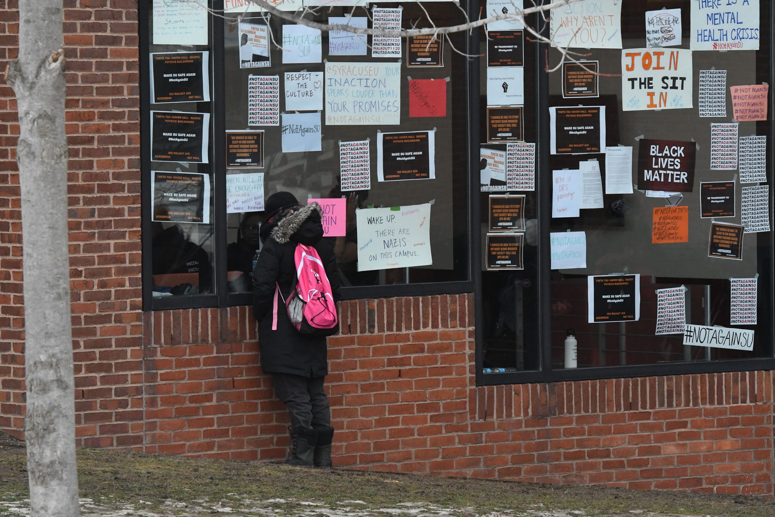 A student presses up against a window of Crouse-Hinds Hall to speak to a friend inside.