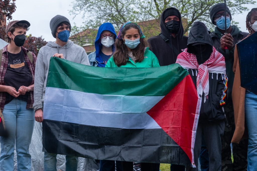 Pro-Palestinian students and faculty hold a press conference in front of the encampment on Shaw Quad at Syracuse university. Students hold a Palestinian flag in solidarity as it rains during the press conference.