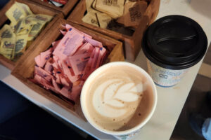 Two coffee cups, one open and one closed, sit next to boxes of sugar packets on a white table.