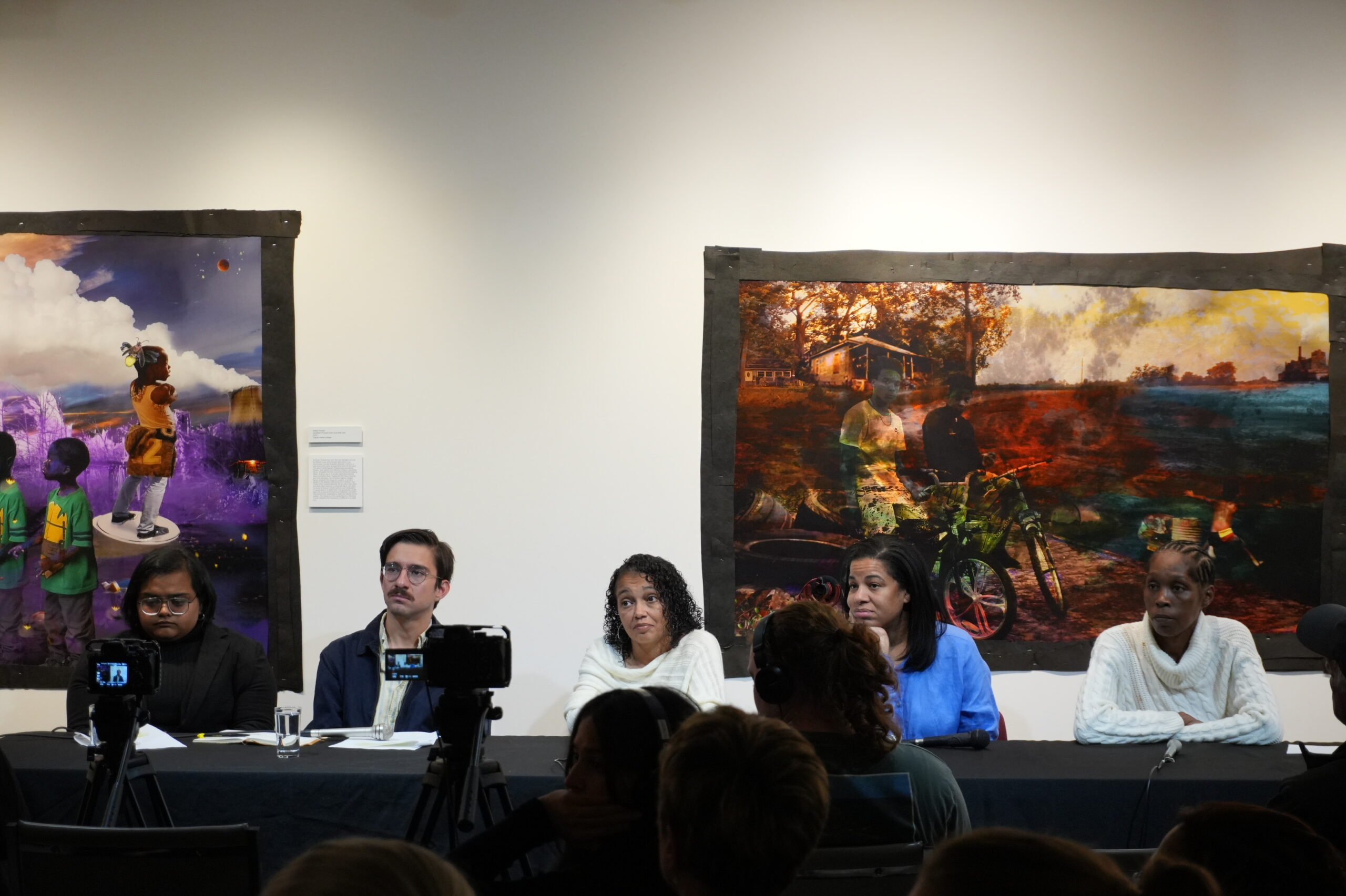 Five people sit at a panel with images on a white wall behind them.