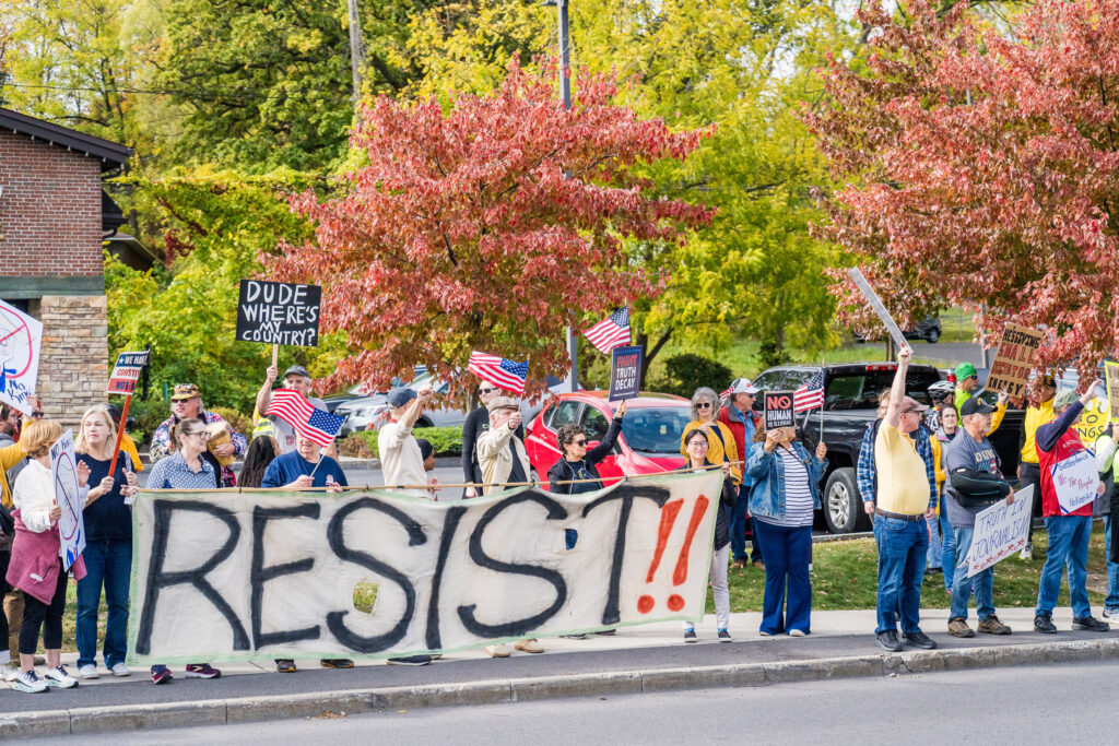 No Kings protestors chant and sing as cars drive by honking their horns along Erie Boulevard in Syracuse on Saturday, Oct. 18, 2025. Protestors brought an assortment of flags and homemade signs.
