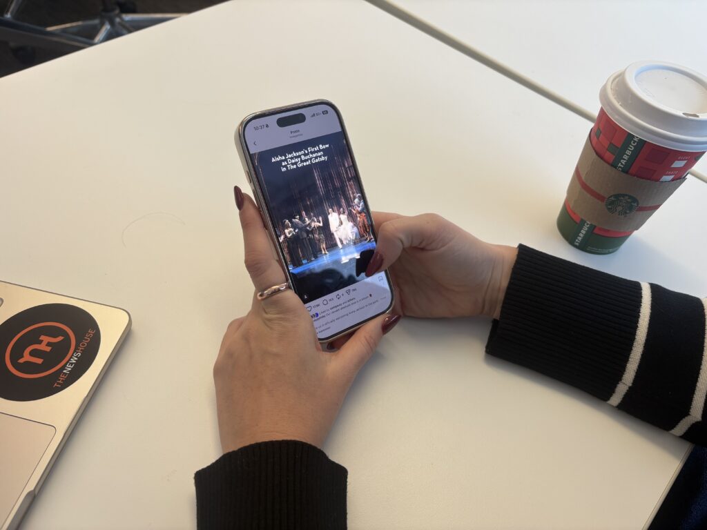 A woman with long nails looks at her phone which is open to Instagram and has an ad for Broadway's 