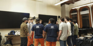 In a classroom, a group of Otto Tunes members stand in a circle holding hands