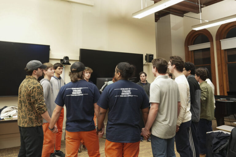 In a classroom, a group of Otto Tunes members stand in a circle holding hands