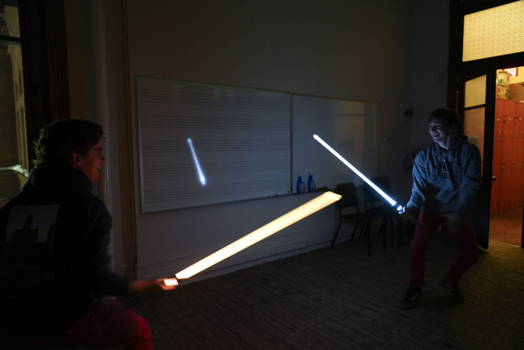 In a dark classroom, two Otto Tune members playfully swing 