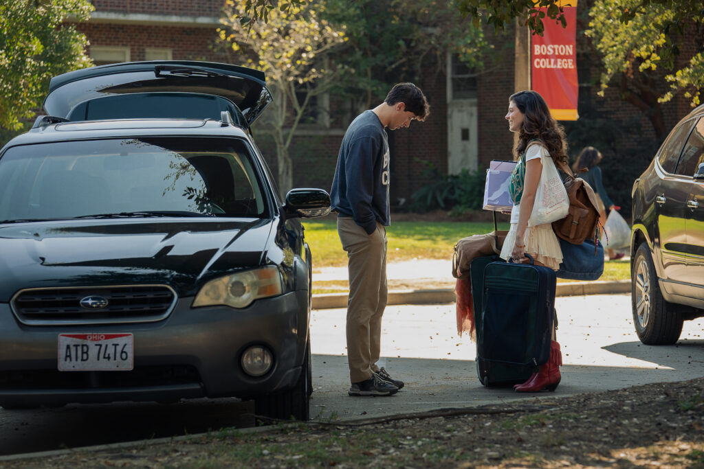 In People We Meet on Vacation, a man in a woman stand in a college parking lot by a car.