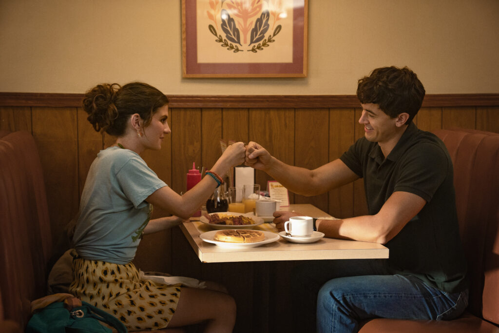 In People We Meet on Vacation, a man and a woman sit at a diner table making a pinky promise.
