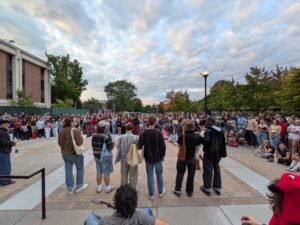 A shot from Syracuse Unversity campus taken on the steps of the library shows men lined up in front of a crowd of almost 100 people.
