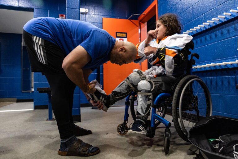 Jamie Favata helps Myles put on his gear before their charity game against the Syracuse men’s club hockey team.