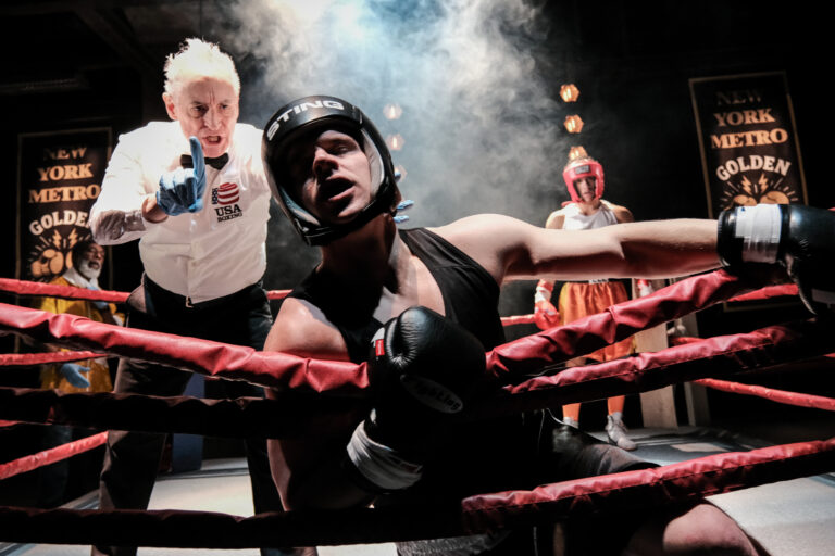In 'Relentless' a man in black boxing attire is knocked out into the red rings as the referee in a white shirt stands above him.