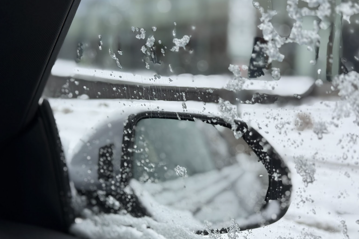 From the inside front window of a car, ice sticks to the outside of the window as the car sits surrounded by snow.