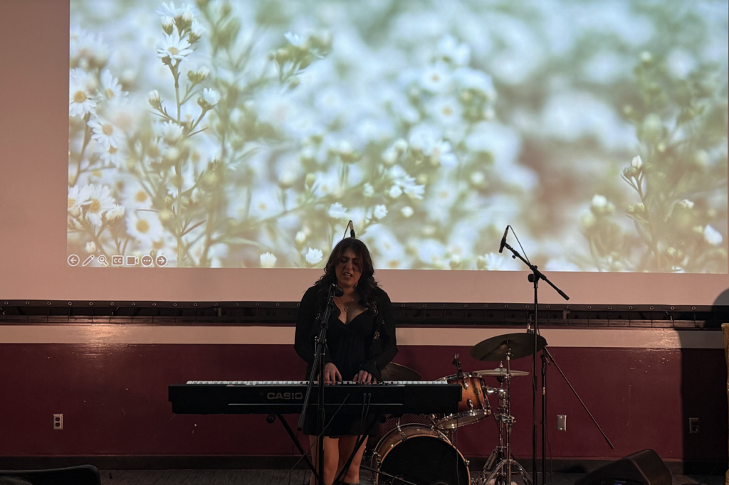 At the first SU Otto Awards, a girl in a black dress performs onstage playing a piano and singing.