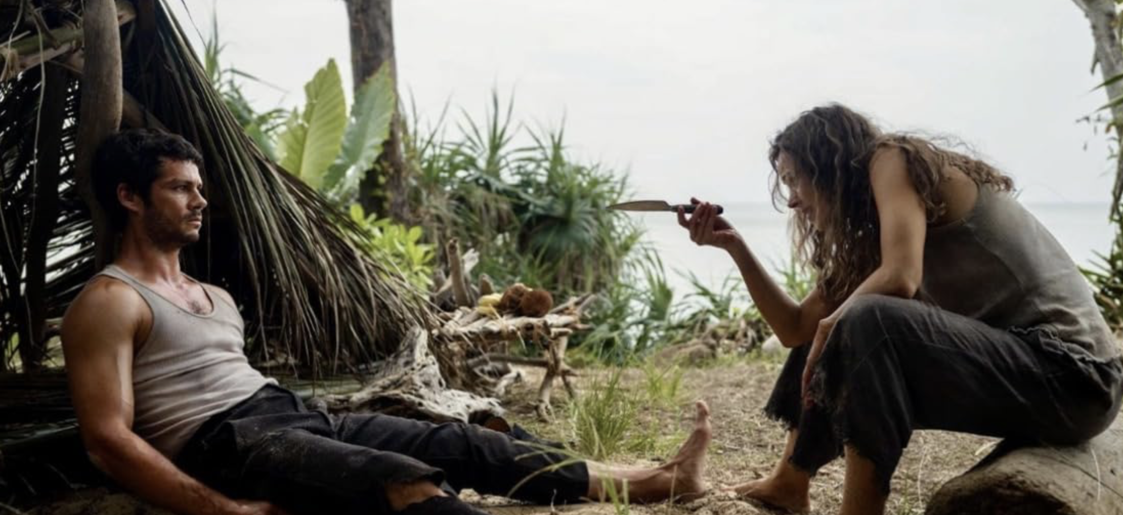 In 'Send Help,' Dylan O'Brien and Rachel McAdams star. In a scene on an abandoned beach, O'Brien sits with an injured leg across from McAdams who is pointing knife at him.