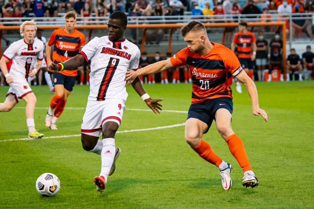 Louisville's Aboubacar Camara (9) has control of possessoin as he winds up for a pass with Syracuse's Max Kent (20) crashing down to defend.