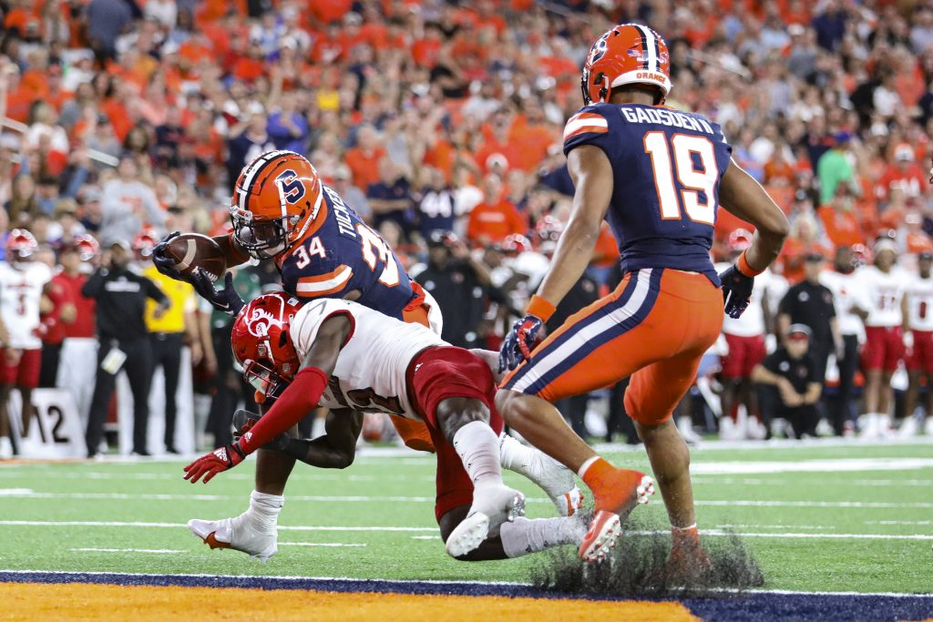 Syracuse's Sean Tucker (34) breaks a tackle from Louisville's Jarvis Brownlee before scoring a touchdown as Orange teammate Oronde Gadsden II (19) looks on.