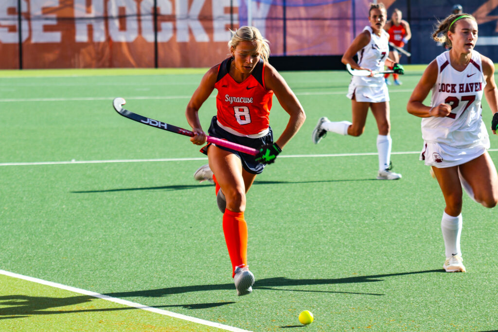 Aiden Drabick (8) in an orange SU jersey runs with possession over the hockey ball during SU's match against Lock Haven on Friday, August. 29, 2025, at J.S. Coyne Stadium.