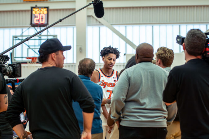A male basketball player is surrounded with reporters and photographers.