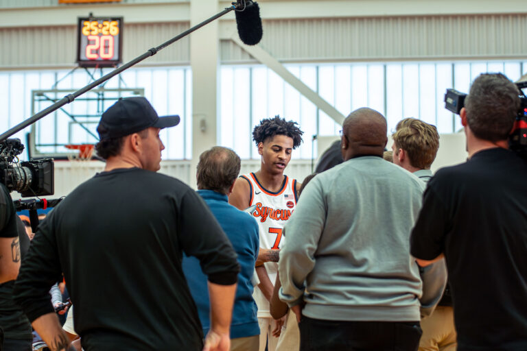 A male basketball player is surrounded with reporters and photographers.