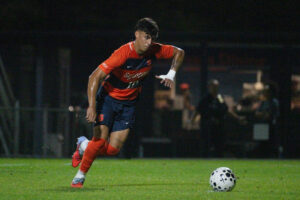 Soccer player in orange and blue runs to kick the ball