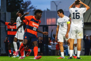 Syracuse soccer player celebrates after a goal. Penn State soccer players react negatively to the goal.