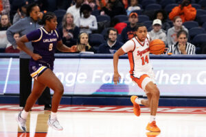 Womens Basketball player in white and orange plays against another womens basketball player in purple and gold.