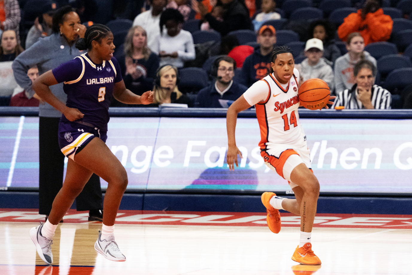 Womens Basketball player in white and orange plays against another womens basketball player in purple and gold.