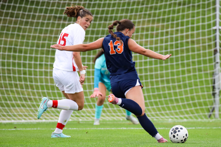 Syracuse female soccer player in blue takes a shot at the goal against a Cornell female soccer player in white