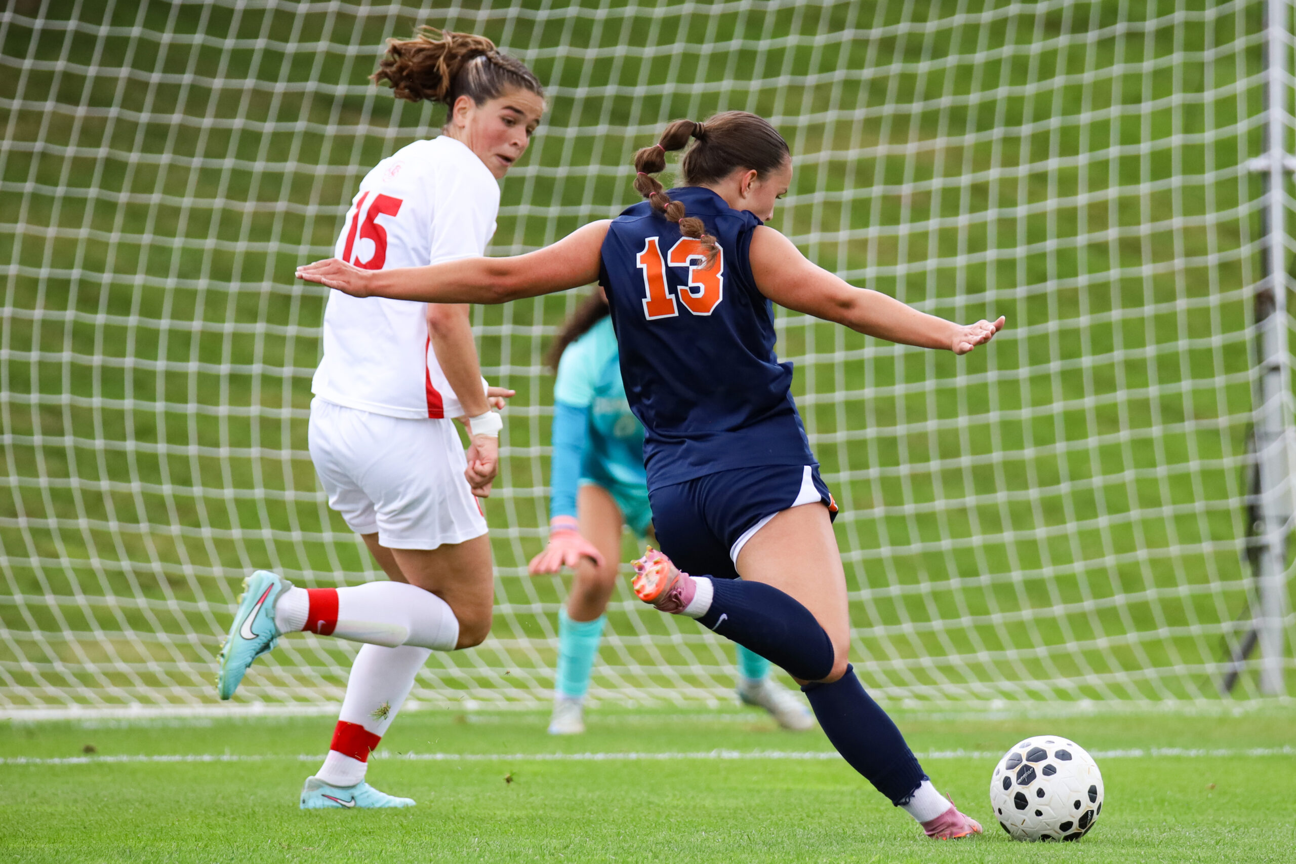 Syracuse female soccer player in blue takes a shot at the goal against a Cornell female soccer player in white