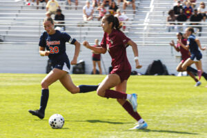 Womens soccer player in maroon races down the field against opposing player in blue.