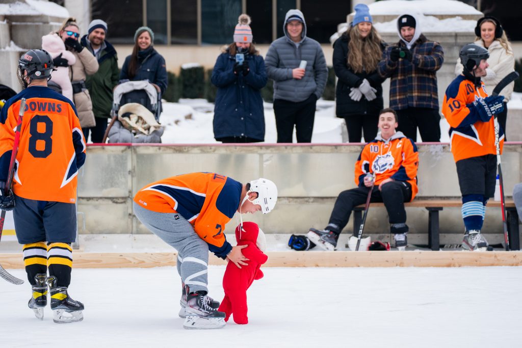 Family and teammates watch as Neal Purcell holds his daughter as she walks on the ice during the Syracuse Pond Hockey Classic at Clinton Square in Syracuse on Jan. 25, 2025.