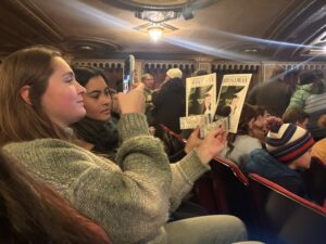 In the Landmark Theater, two young women hold up their "Wicked" programs and tickets in front of the stage to take a picture.